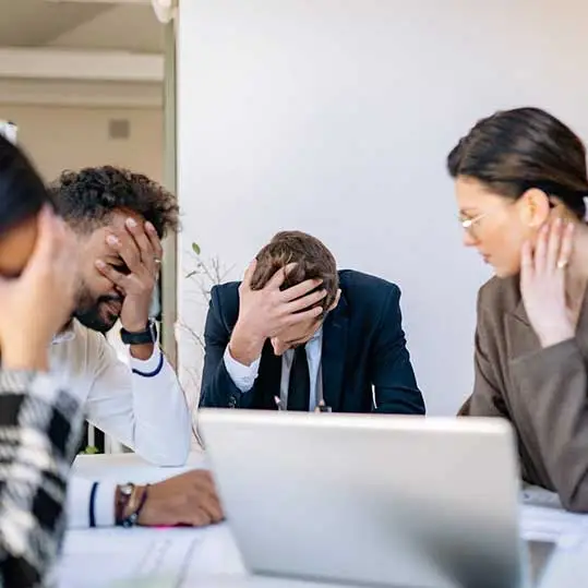 A frustrated business team sitting around a laptop, overwhelmed by technical issues — a visual representation of how poor website performance can hurt productivity and client trust.